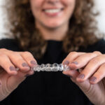 Joven caucásica mostrando un alineador invisible de silicona para la corrección dental. Mano femenina sosteniendo los retenedores dentales de plástico para enderezar los dientes.